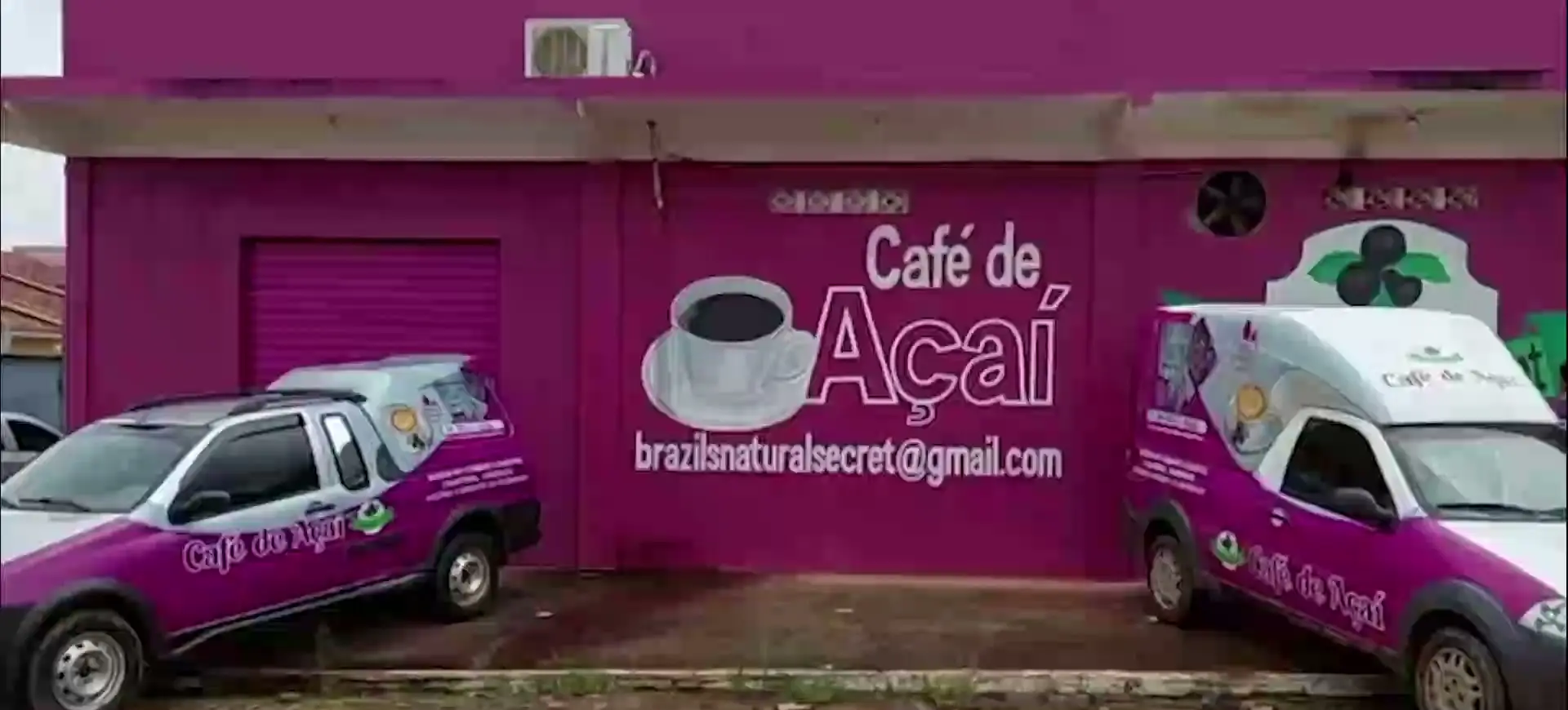The factory in Itupiranga, magenta frontage painted with the company logo, two branded delivery pickups parked outside.