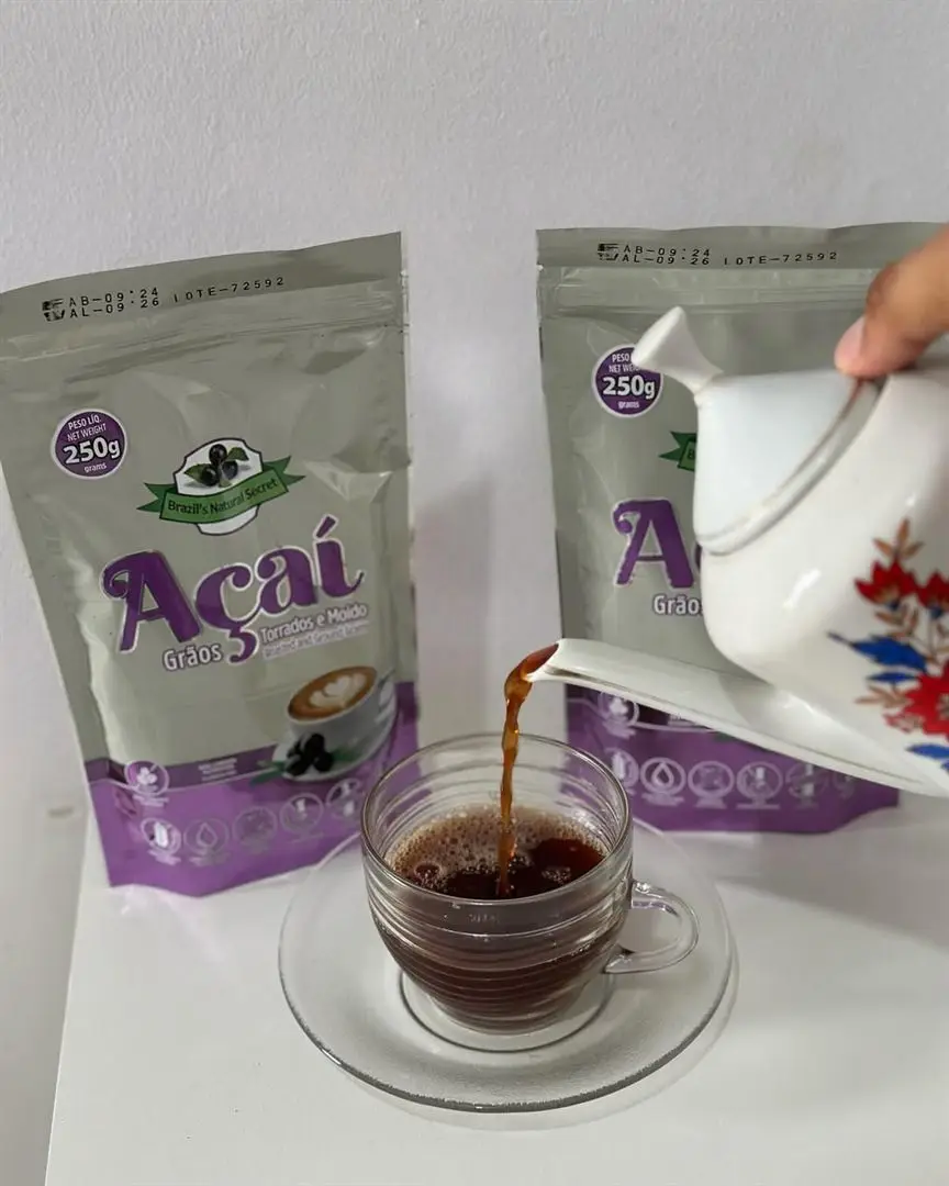 Açaí seed coffee being poured into a glass cup, with two 250 g pouches behind it.
